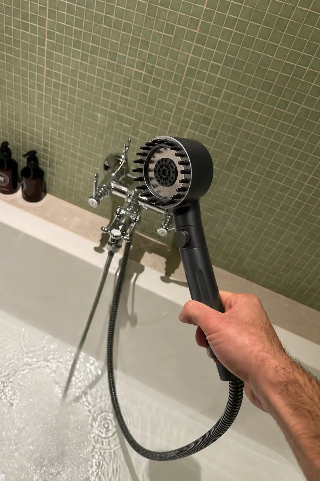 Hand holding a black RAINLY shower head above a bathtub