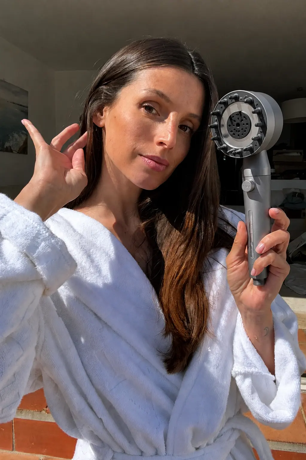 Customer in a robe holding a gray RAINLY filtered shower head